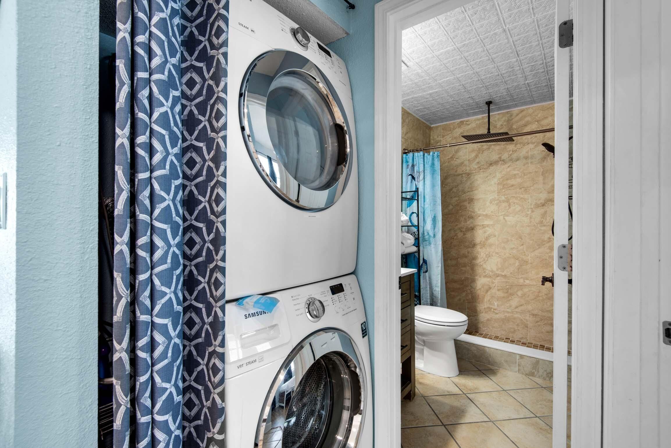 A laundry area with a front-loading washer and dryer, a bathroom with a toilet and shower, and a door leading to another room.