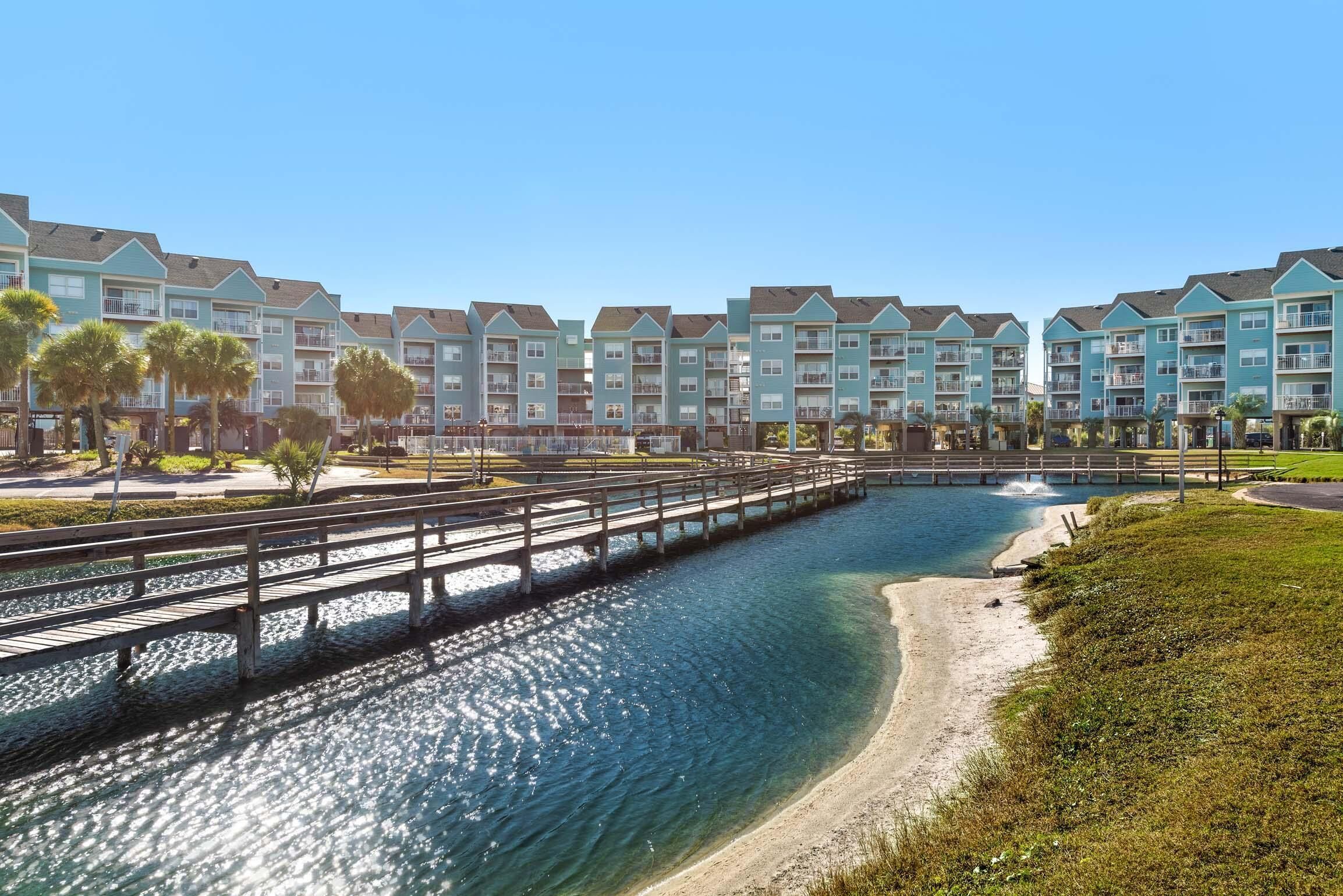 A waterfront hotel with multiple-story buildings, a wooden bridge, and a clear blue pool.