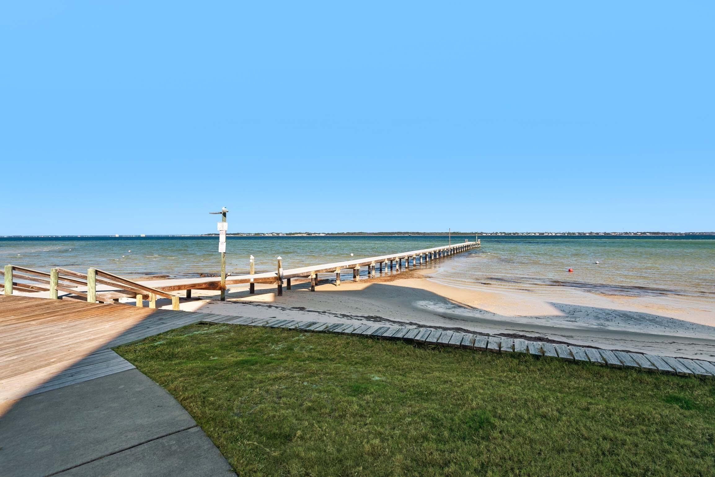 A wooden boardwalk leading to a beach with a grassy area in the foreground.