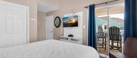 Un dormitorio con una cama grande, ventilador de techo, televisor y vistas al balcón.