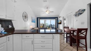 A kitchen with white cabinets, a dark countertop, and a ceiling fan. There is a dining area with a table and chairs.