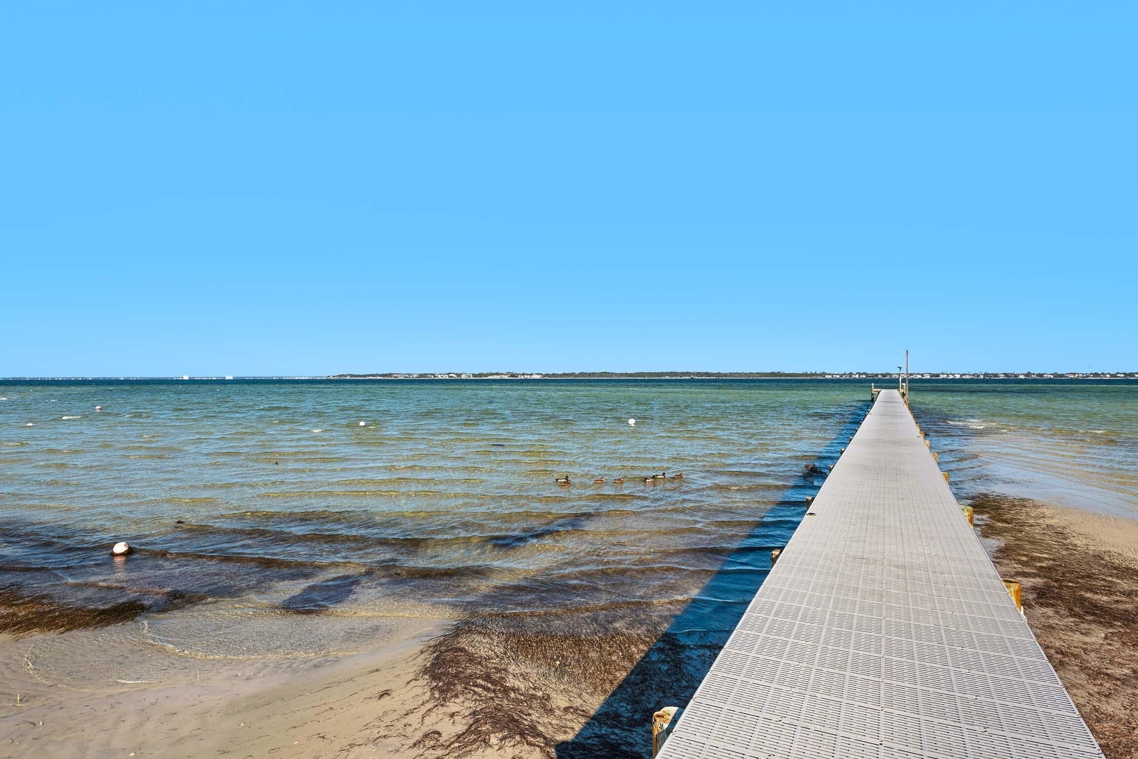 A long, narrow concrete pier extending into a calm body of water, with clear skies above.