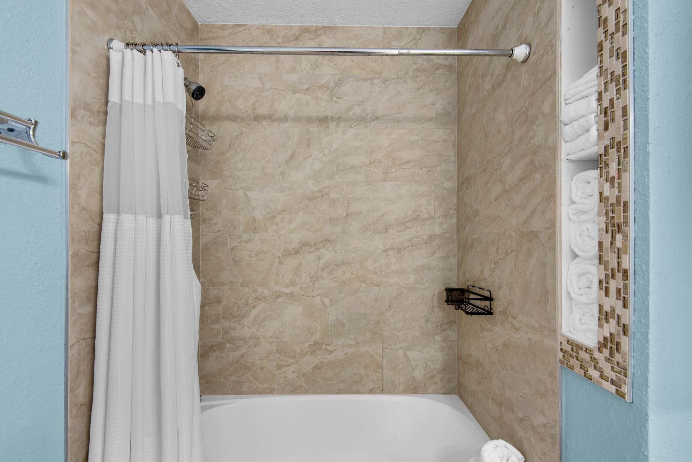 A shower area with a bathtub, beige tiled walls, a shower curtain, and a towel rack with towels.