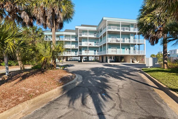 A multi-story hotel with balconies, palm trees, and a parking lot. - Baywatch F9 (Pensacola Beach)