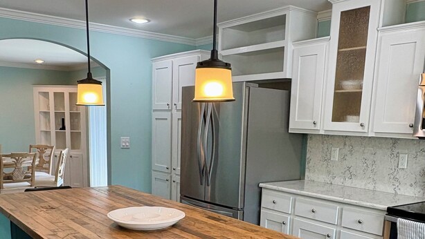 A kitchen with a wooden island, bar stools, white cabinets, and stainless steel appliances. - Oasis at Muchy Branch (Rehoboth Beach)