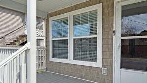 A front porch with a wooden deck, a white railing, and a sliding glass door. - Oasis at Muchy Branch (Rehoboth Beach)