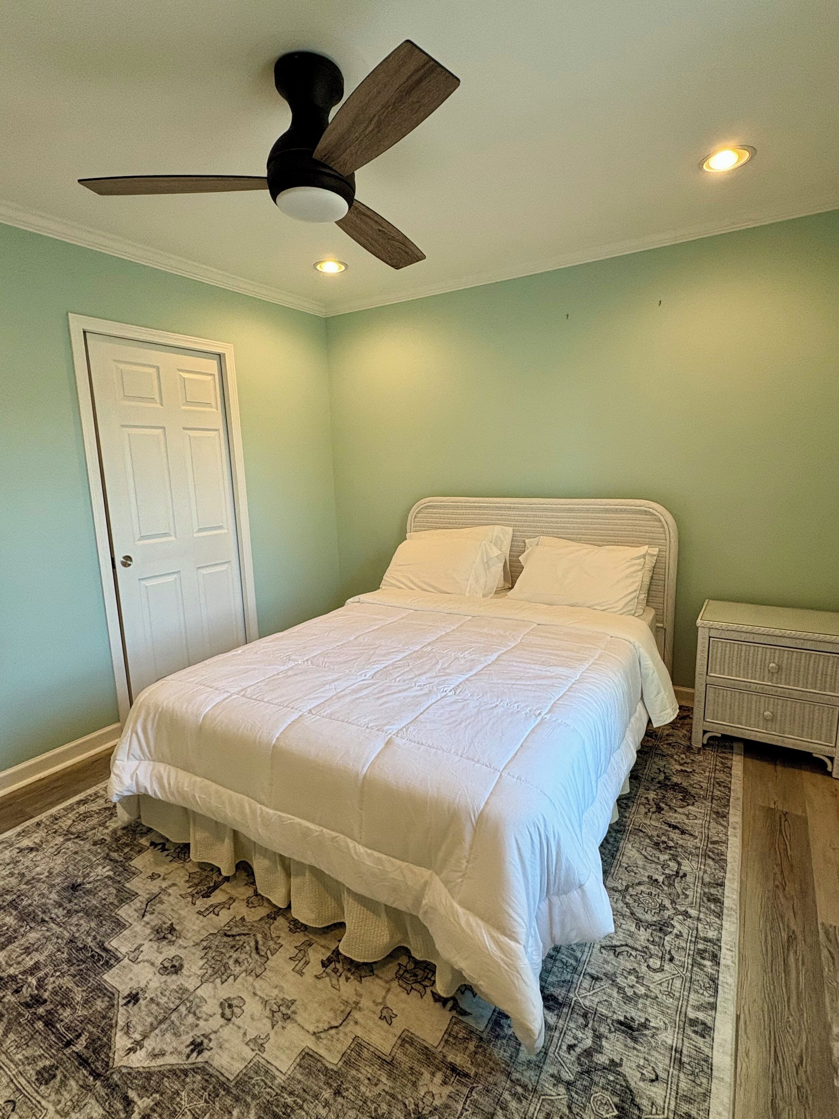 A bedroom with a bed, a ceiling fan, a door, and a nightstand.