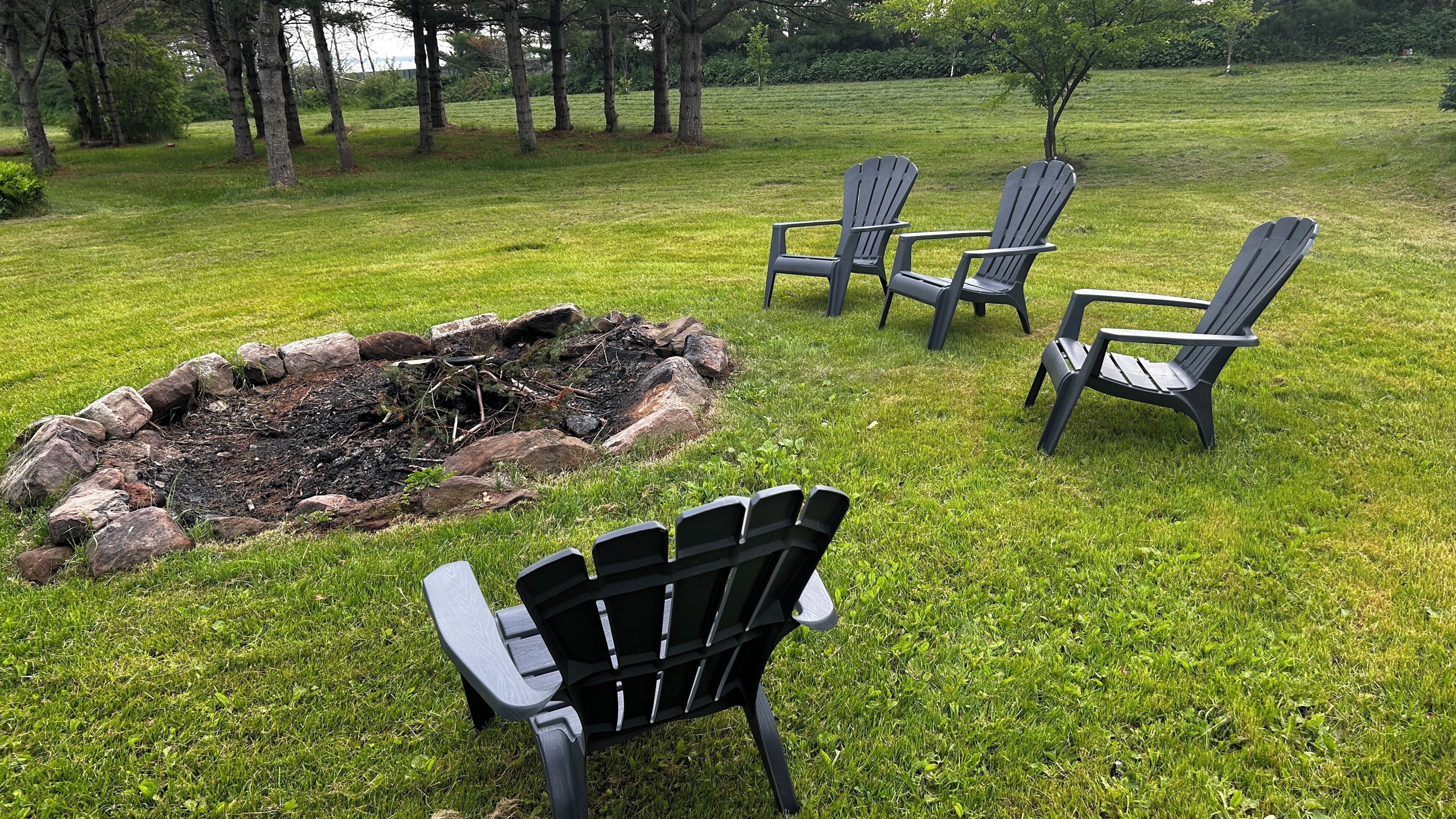 Een gazon met een vuurkorf en vier Adirondack-stoelen.