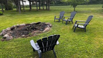 Een gazon met een vuurkorf en vier Adirondack-stoelen.