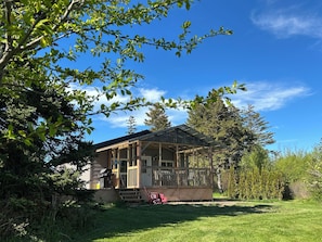 Eine Holzhütte mit Veranda, umgeben von Bäumen und blauem Himmel.