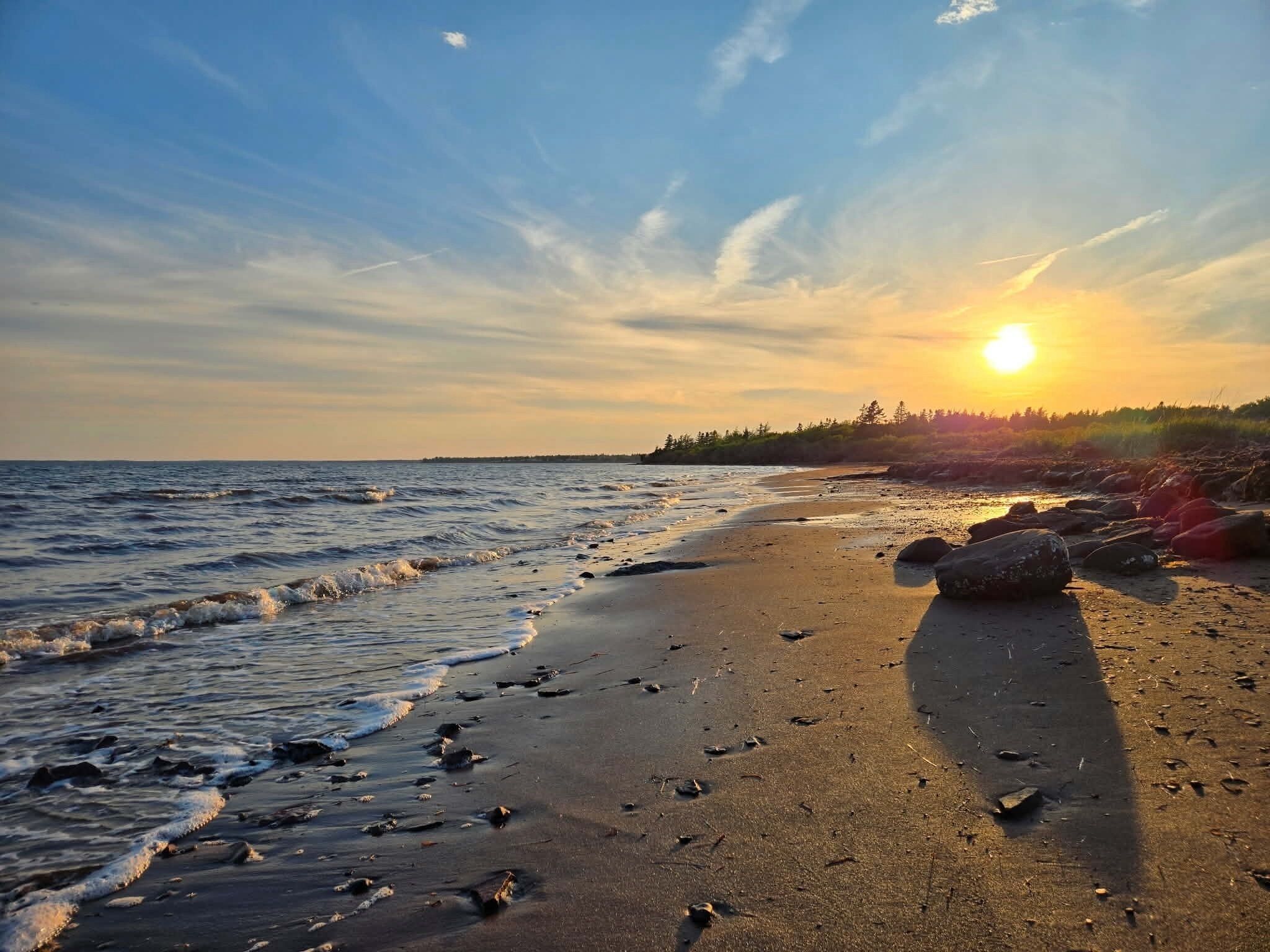 Een strand met golven, een zonsondergang en een verre kustlijn.