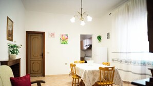 Zona pranzo con tavolo apparecchiato per quattro, circondato da sedie, un lampadario e una porta che dà su una cucina.
