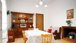 Zona pranzo con tavolo apparecchiato per quattro, sedie in legno, forno a microonde e pensile con vetrine.