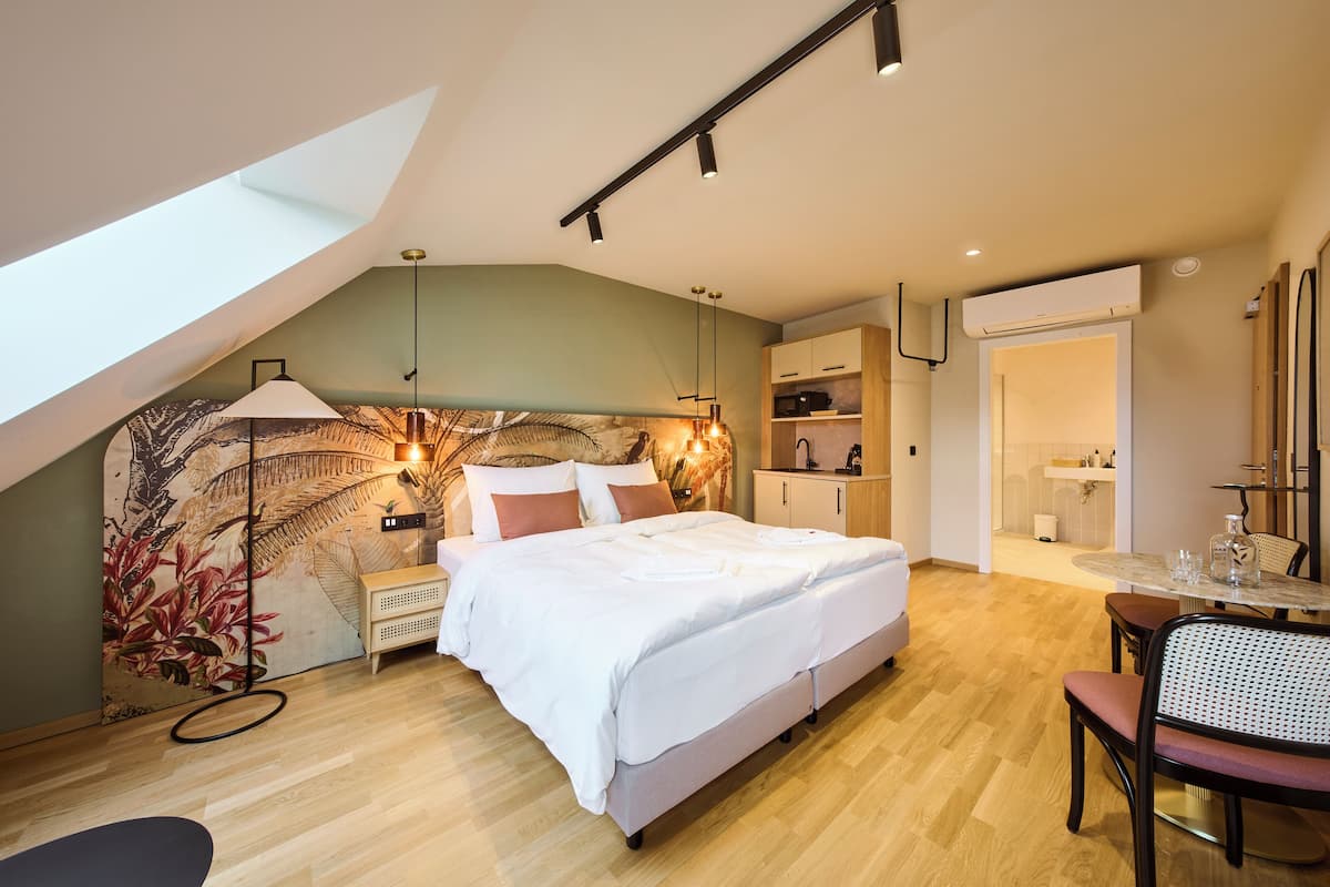 Un dormitorio con tragaluz, cama, mesita de noche, silla, escritorio y baño con espejo y lavamanos.