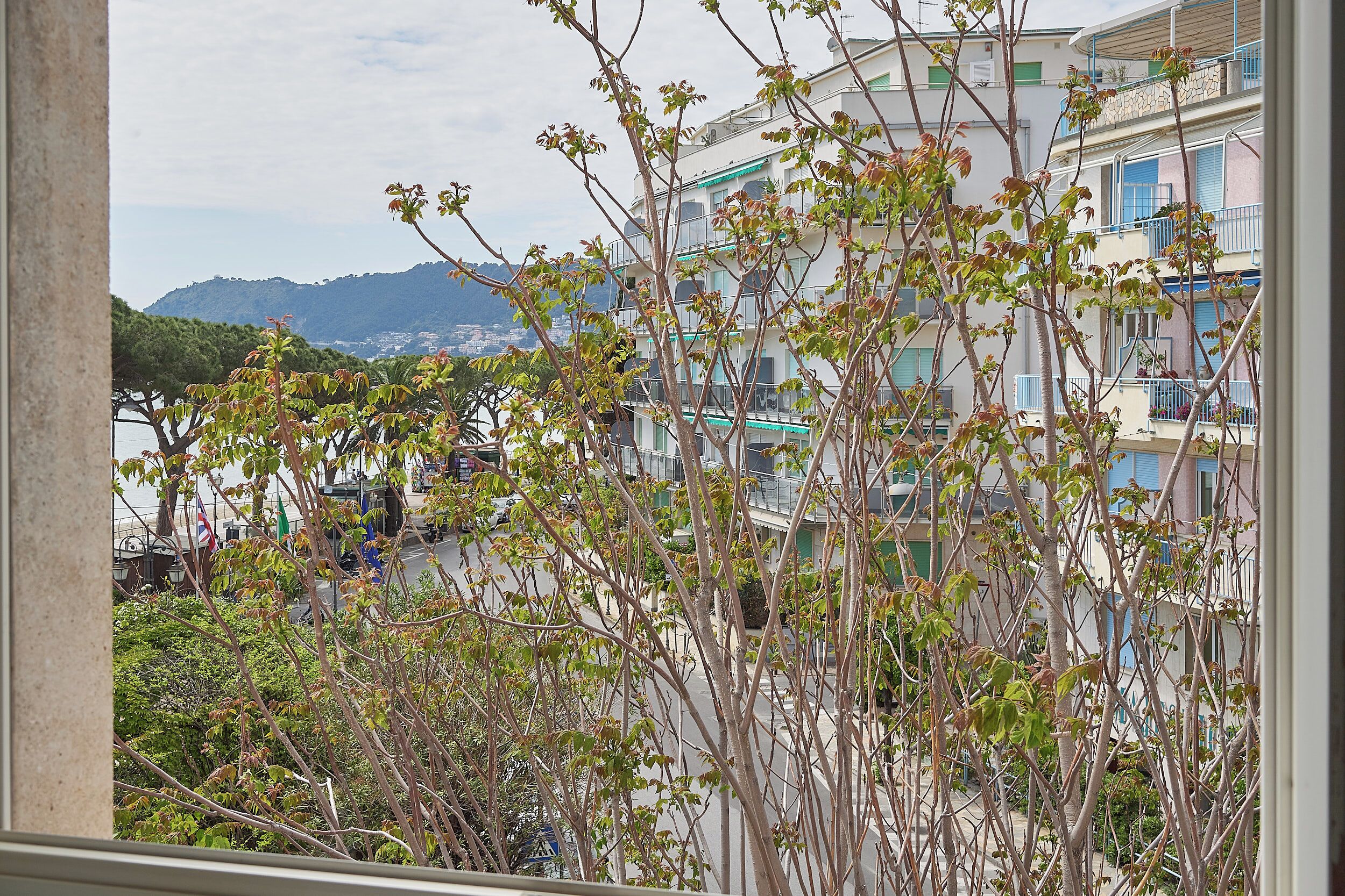 A view of a multi-story building with balconies, a street in the foreground, and a mountainous landscape in the background.