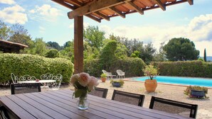 A wooden table with a vase of flowers, outdoor seating, and a pool in the background. - Beautiful detached villa on one level with pool, view and charging station! (La Cadière-d'Azur)
