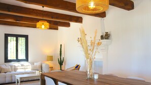 A modern living room with a wooden dining table, white chairs, a sofa, and a fireplace. - Beautiful detached villa on one level with pool, view and charging station! (La Cadière-d'Azur)