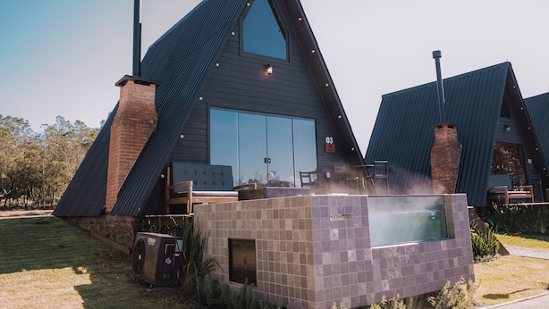 Un bâtiment moderne, doté d’un toit triangulaire, d’une grande fenêtre en verre, d’une cheminée en briques et d’un petit espace extérieur aménagé pour s’asseoir.