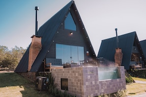 A modern, triangular-roofed building with a large glass window, a brick chimney, and a small outdoor seating area. - Vila Gramado (Gramado)