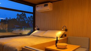 Une chambre moderne avec deux lits, un canapé, une petite table et une fenêtre donnant sur des arbres et des immeubles.