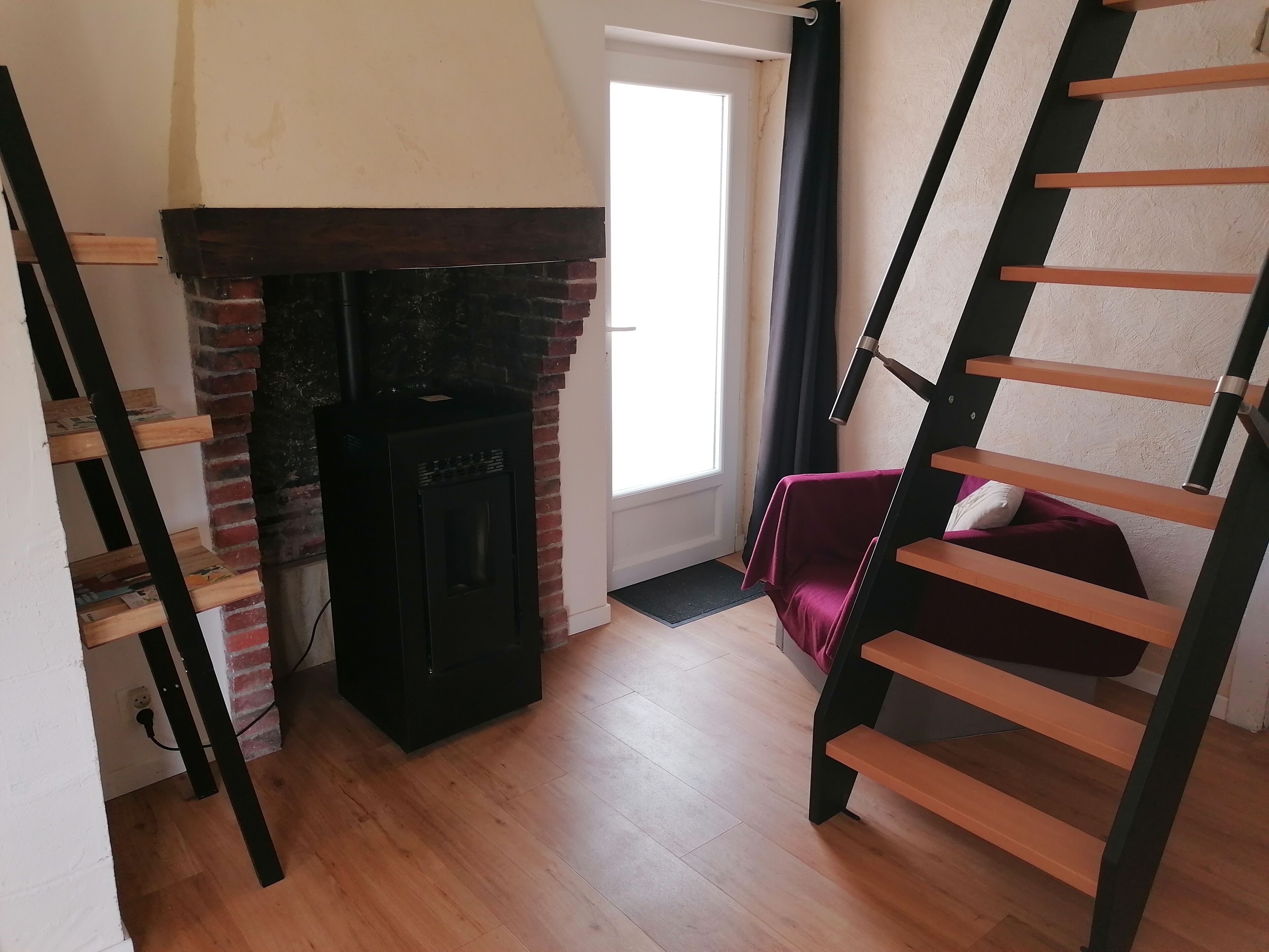 A room with a brick fireplace, a wooden staircase, and a bed with a red blanket.