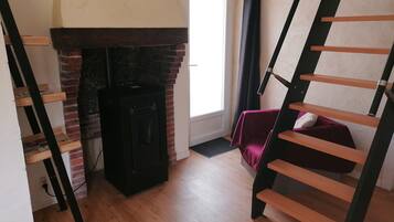 A room with a brick fireplace, a wooden staircase, and a bed with a red blanket.