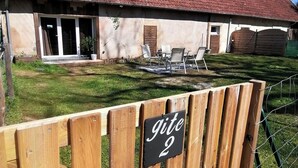 A rustic building with a tiled roof, a wooden gate labeled "gite 2", and a small outdoor seating area with chairs and a table. - FARMHOUSE GITE WITH SHARED POOL - A CHANGE OF SCENERY FOR FAMILY AND FRIENDS (Cachen)