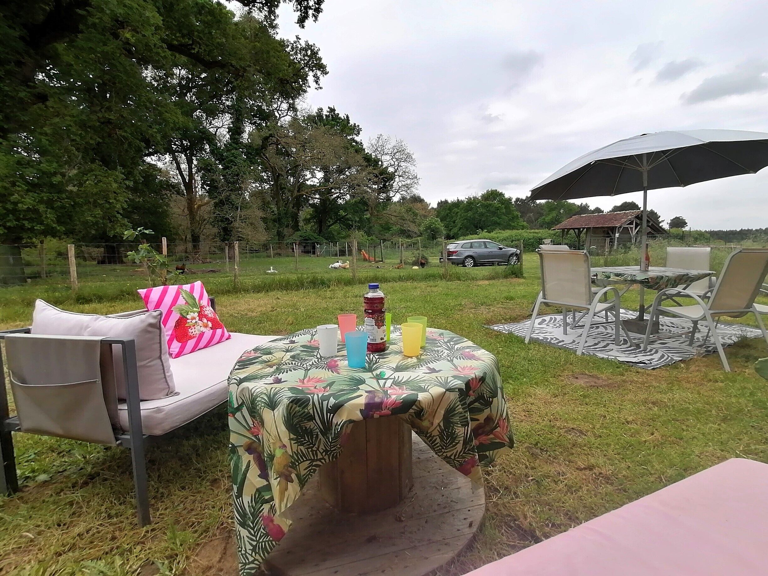 Un área de estar al aire libre con una mesa redonda cubierta con mantel floreado, rodeada de sillas y un paraguas grande.