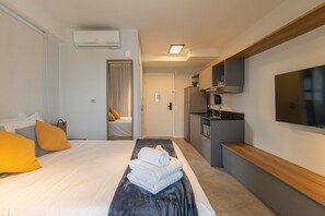 A hotel room with a bed, a desk, a kitchenette, and a TV.
