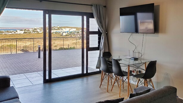 A modern living room with a balcony, a flat-screen TV mounted on the wall, and a dining area with a table and chairs. - NIVICA Lifestyle Living 20, Langebaan 4-Sleeper (Langebaan)