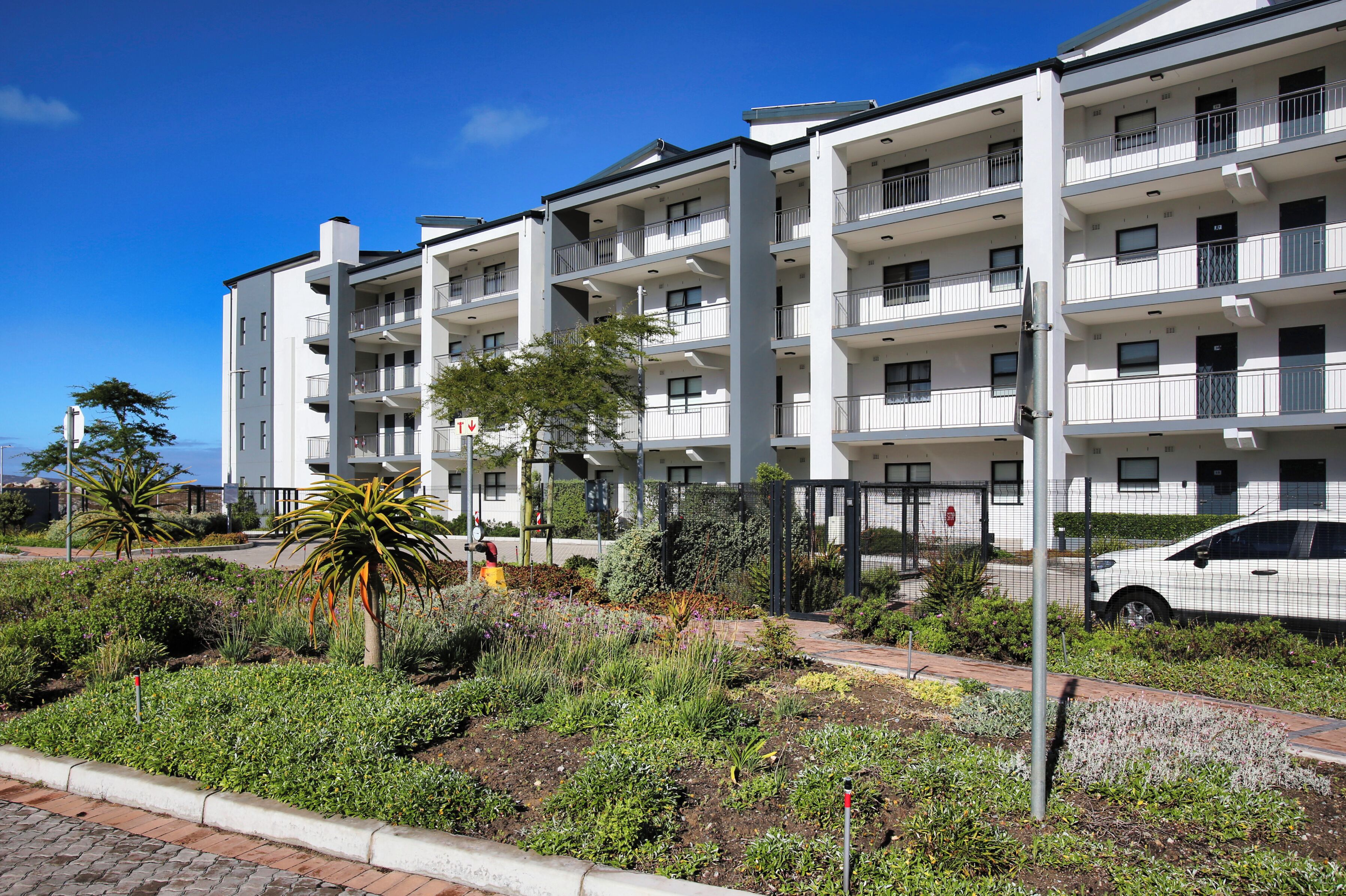 A multi-story residential building with balconies, a paved walkway, and a garden area.