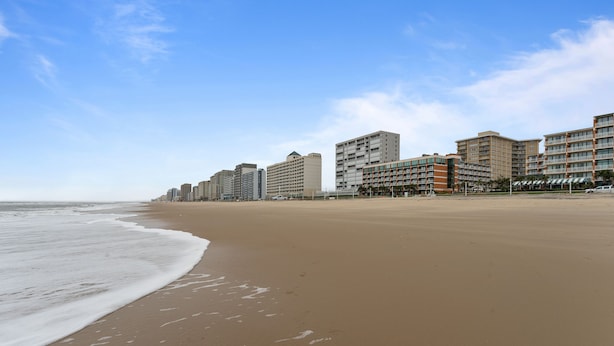 Ein weiter Sandstrand mit einer Reihe mehrstöckiger Gebäude im Hintergrund.