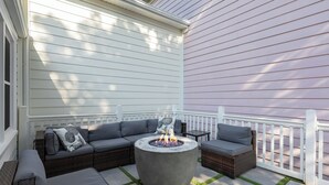 Eine Terrasse mit Feuerstelle, grauer Gartenmöbel und einem weißen Zaun.