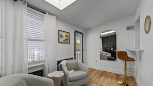 Ein modernes Wohnzimmer mit Sofa, Sessel, rundem Tisch und Barhocker.