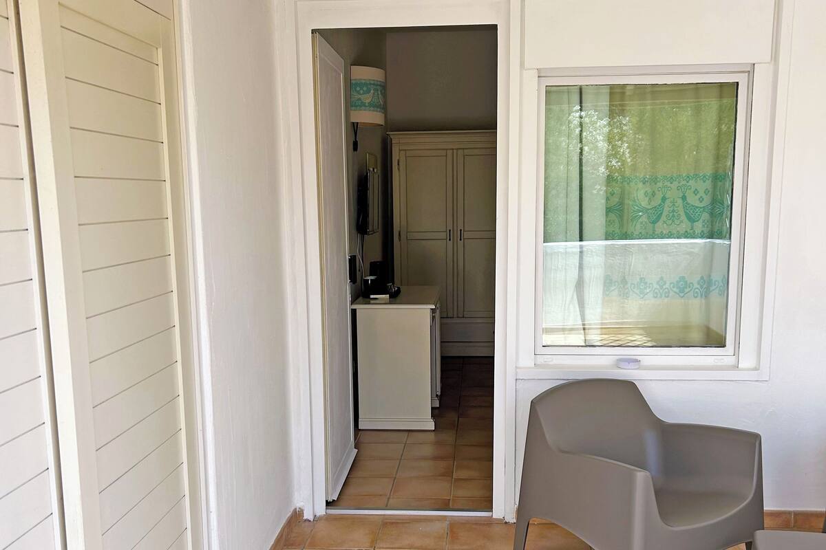 Ein kleiner Raum mit Fliesenboden, einem Fenster mit Vorhängen, einem Stuhl und einem kleinen Tisch.