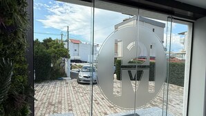A modern building entrance with a glass door reflecting the sky and a parking area. - Shehu Villa Ksamil (Ksamil)