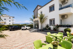 A hotel with a paved courtyard, outdoor seating, and parked cars. - Shehu Villa Ksamil (Ksamil)