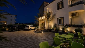 Hotel com pátio pavimentado, área de estar externa e um carro branco estacionado na frente.