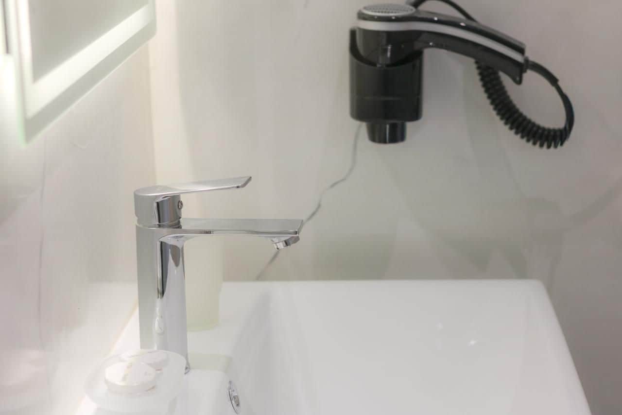 A bathroom with a chrome faucet, a white sink, and a hairdryer mounted on the wall.