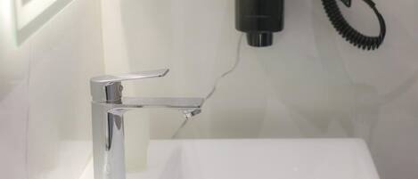A bathroom with a chrome faucet, a white sink, and a hairdryer mounted on the wall.