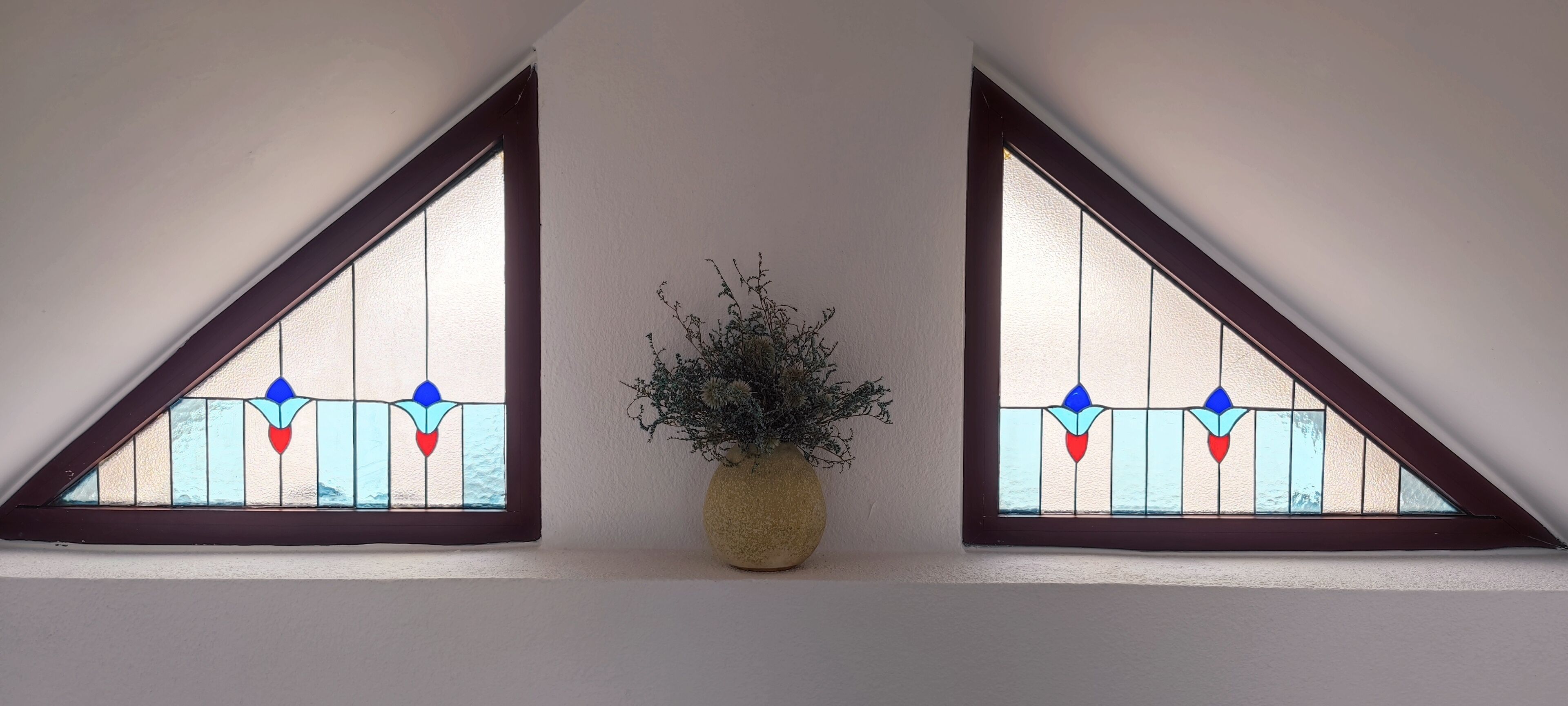 Two triangular stained glass windows with a potted plant in between.