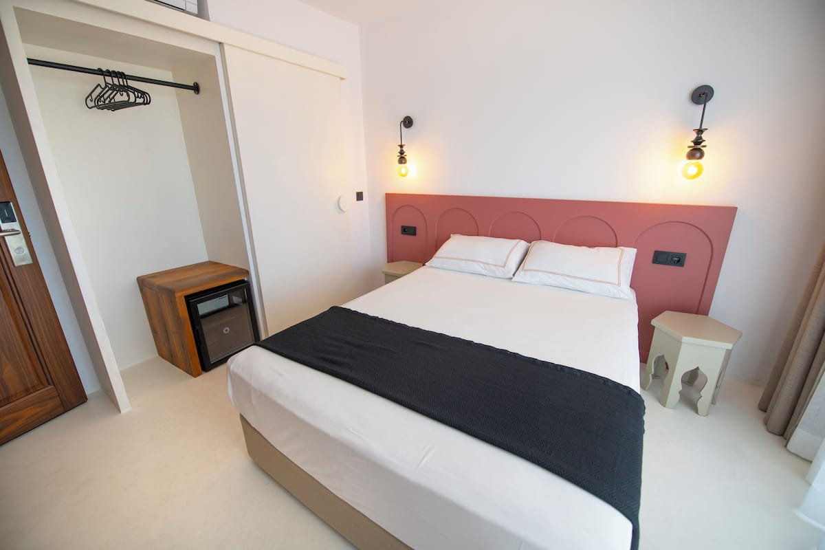 Un dormitorio con cama, mesitas de noche, armario y perchero.