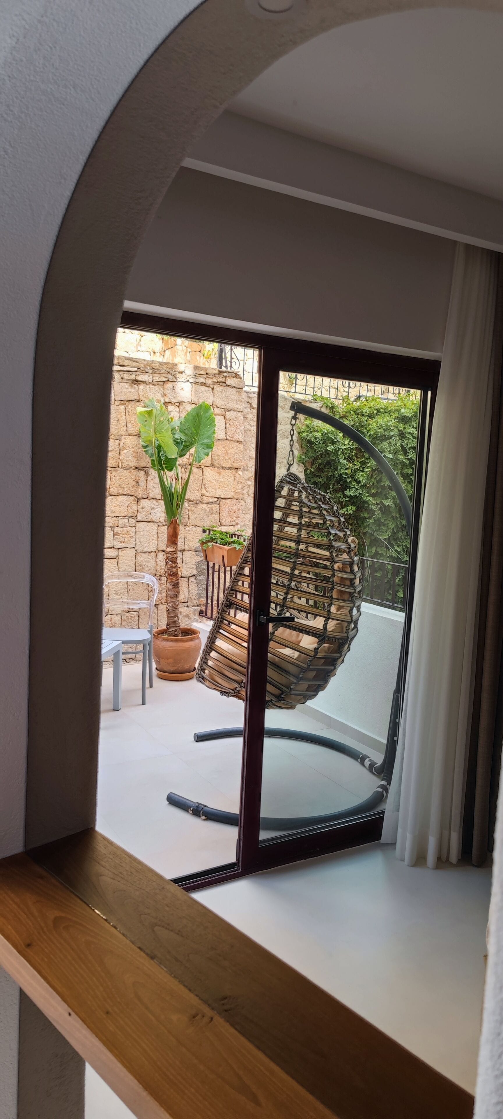 Uitzicht vanaf een balkon met een rieten hangstoel, een bloempot en een stenen muur.