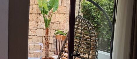 Uitzicht vanaf een balkon met een rieten hangstoel, een bloempot en een stenen muur.
