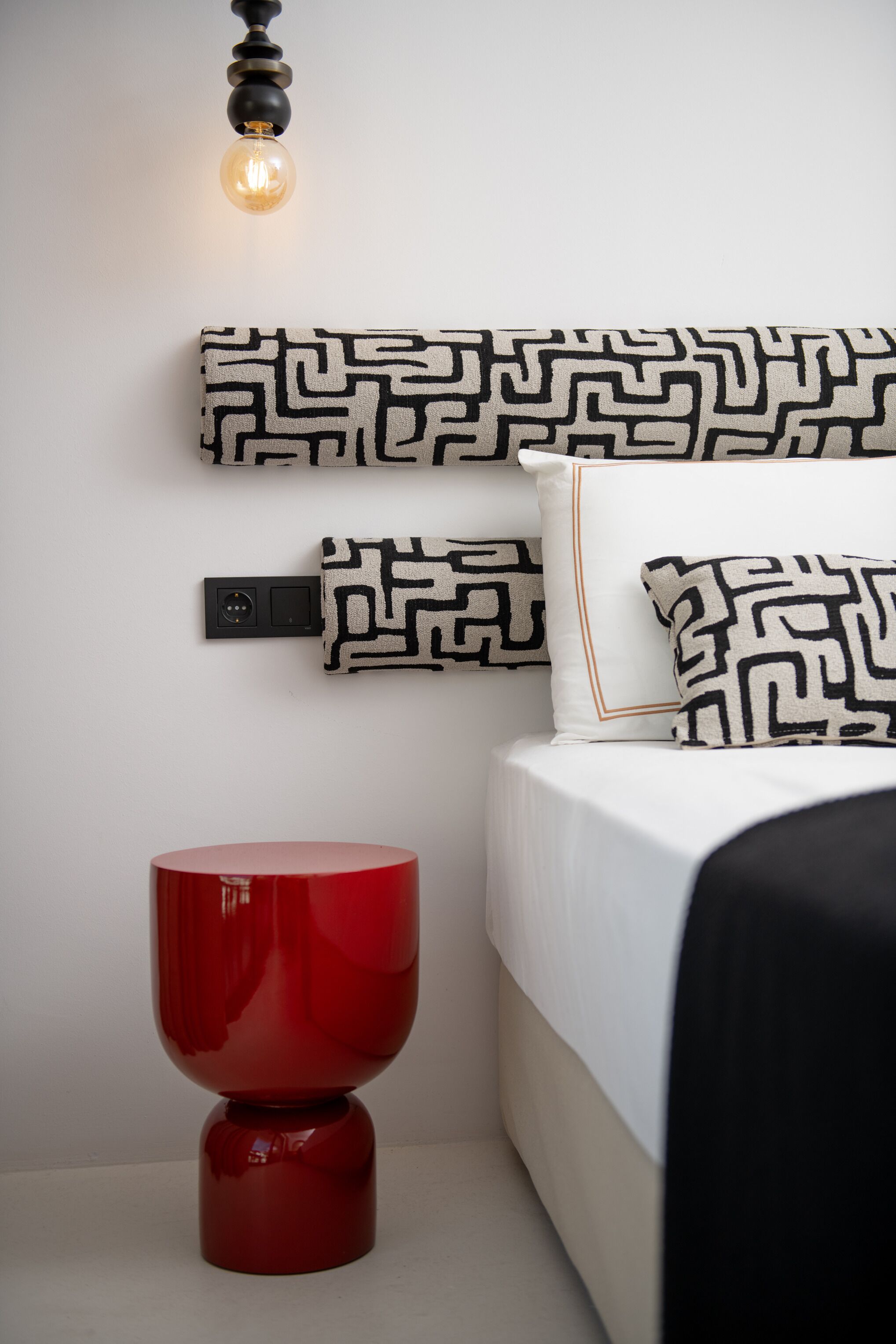 A modern bedroom with a bed, a red side table, and a wall-mounted light fixture.