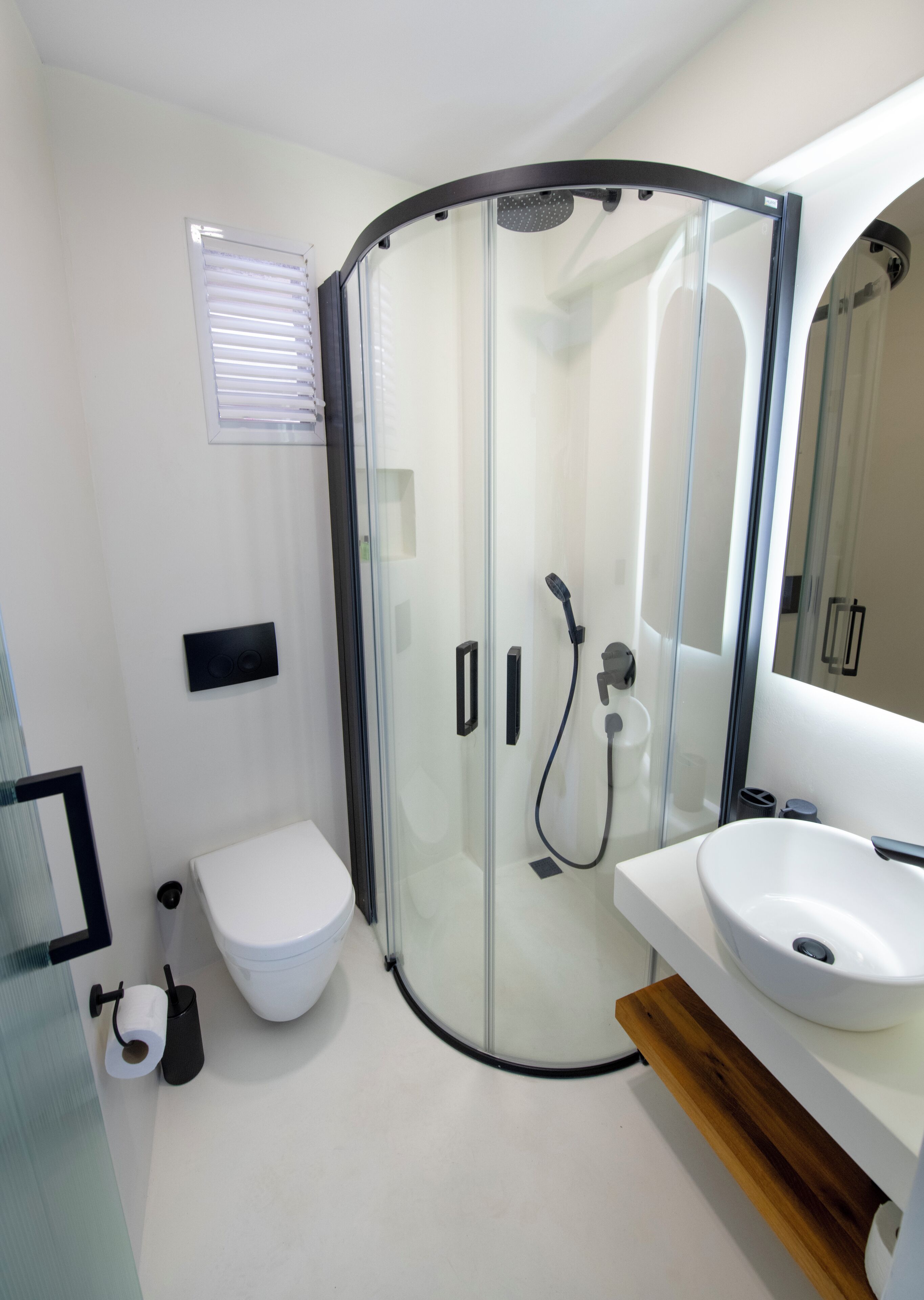 A modern bathroom with a glass-enclosed shower, a toilet, a sink, and a toilet paper holder.