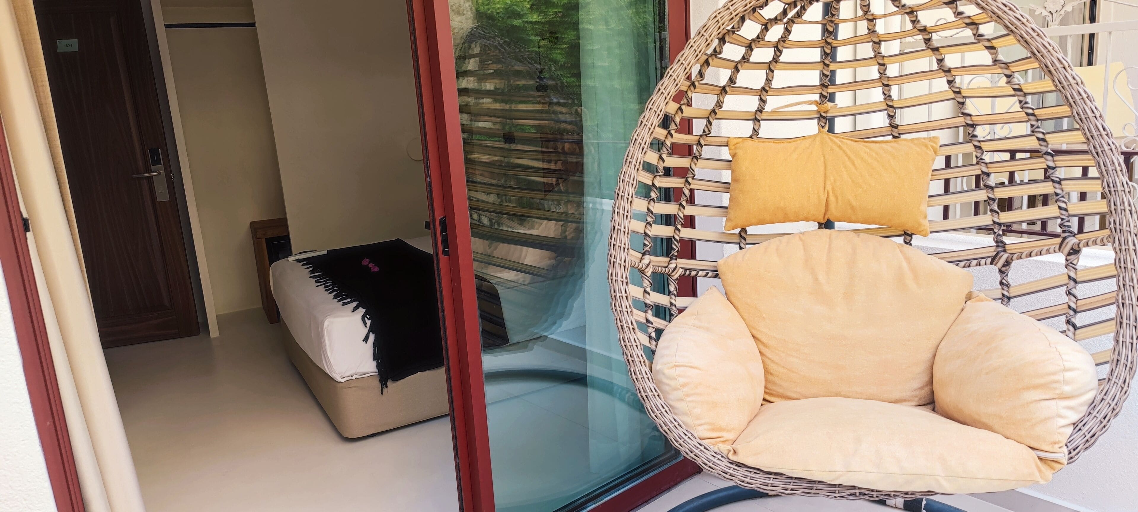 A room with a wicker hanging chair, a sofa, and a glass door leading to a balcony.