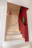 Una escalera con escalones blancos y barandilla roja, con una pequeña planta a la derecha.