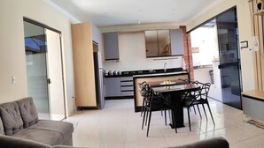 A modern kitchen with a dining area, a sofa, and a sliding glass door leading to a balcony. - House with HEATED POOL (No additional cost) (Bopiranga Itanhaém)