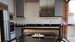 A modern kitchen with a central island, black chairs, and a tiled floor. - House with HEATED POOL (No additional cost) (Bopiranga Itanhaém)